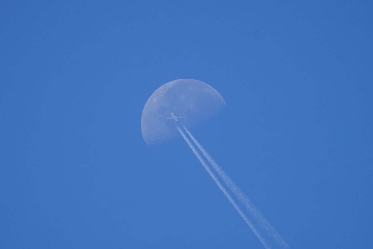 Airliner with twin contrails crossing the lower edge of the daytime moon