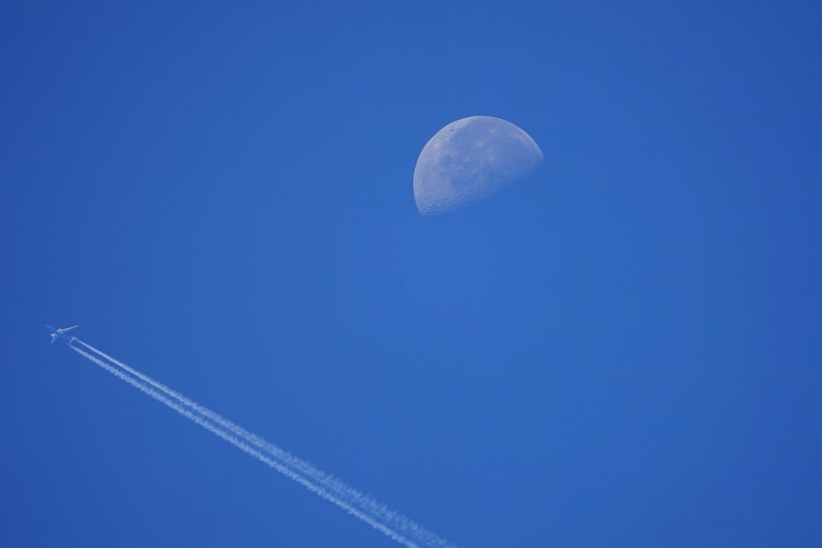 Airliner with long twin contrails passing beneath the daytime moon