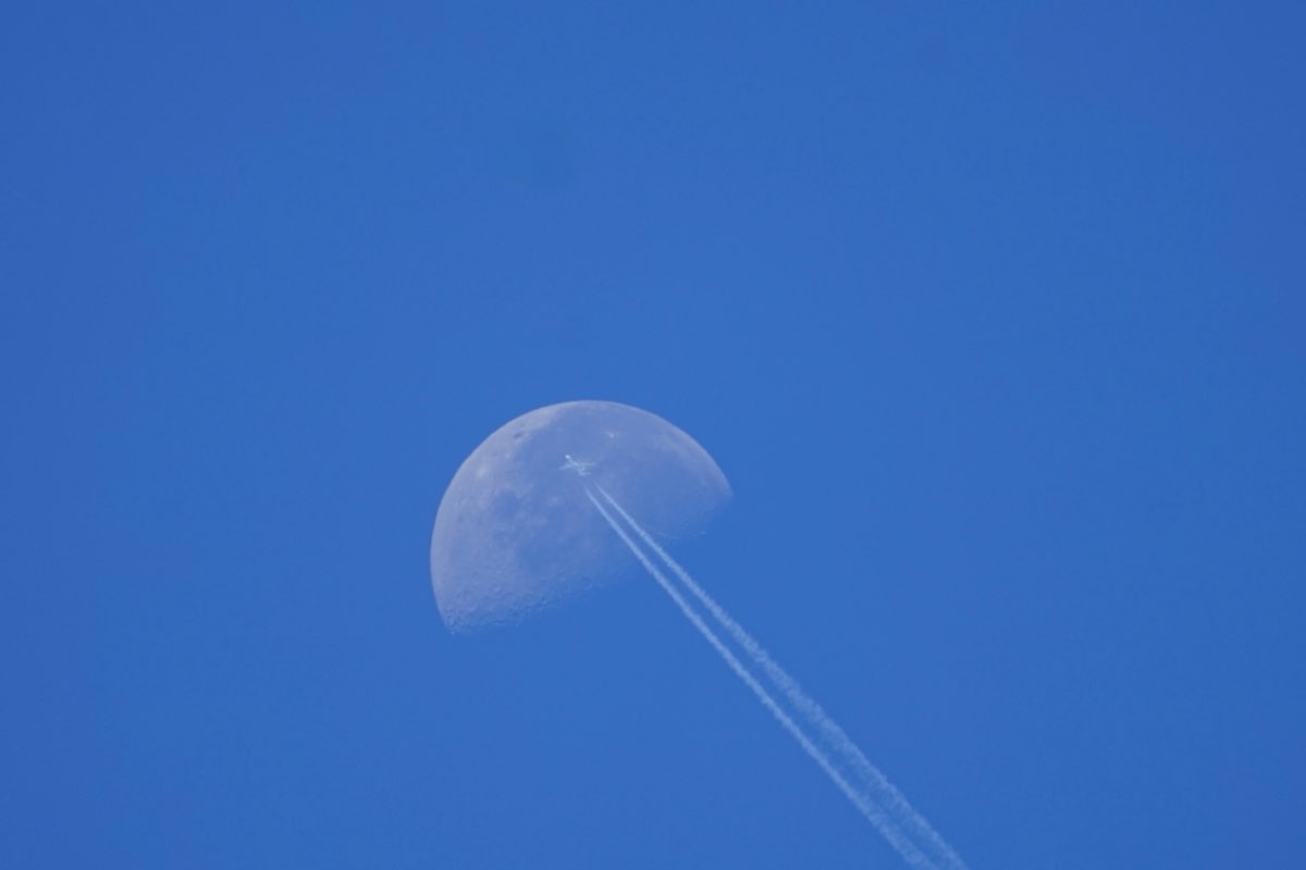 Airliner on the upper face of the daytime moon, twin contrails streaming down to the right